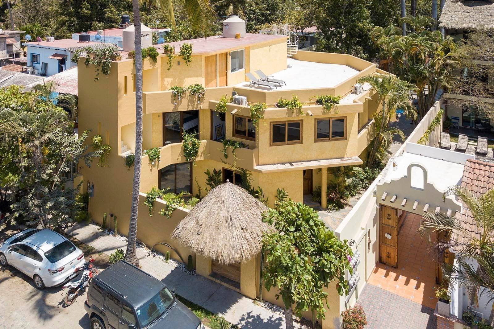Casa Di Giulio from above: the ochre building with a thatched palapa at the entrance, among palm trees